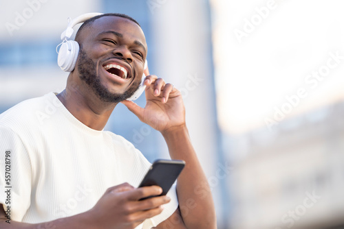 Happy black man smiling listening to music looking at the phone in the street photo
