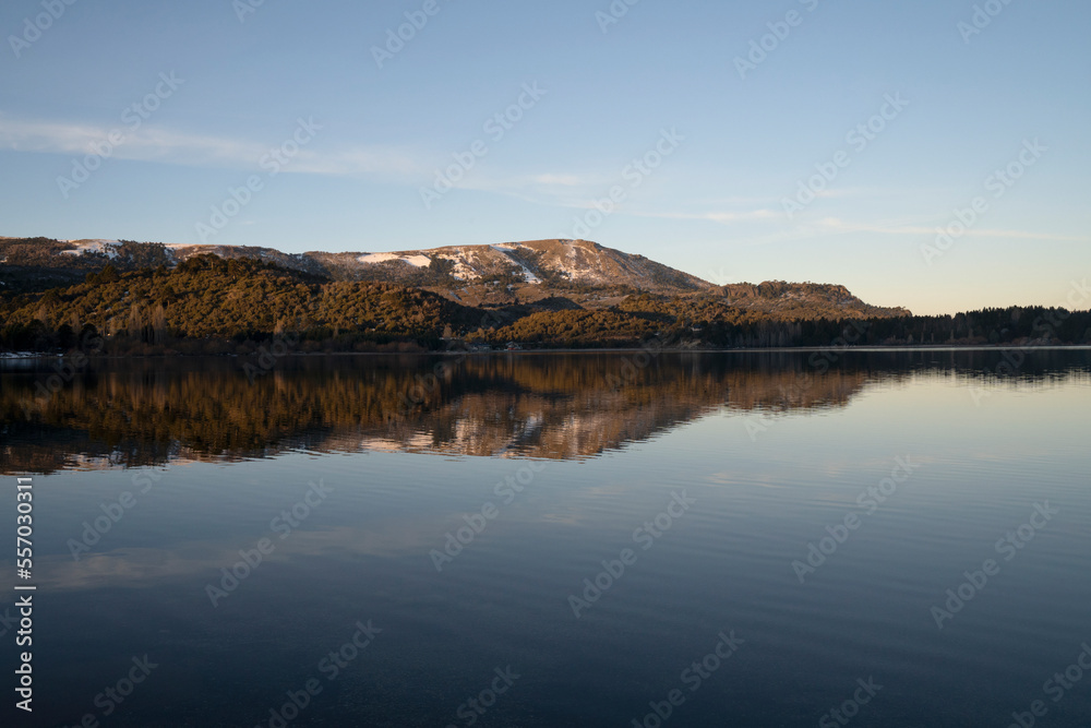 Serene landscape. View of the calm lake, mountains and forest at sunset. The blue sky and environment reflection in the water surface. 