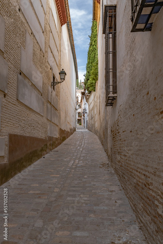 Granada, Spain, 21st of October, 2022. On the way to the Alhambra Palace. Carrera Del Darro street with small souvenir shops and walking tourists. Narrow cobbled street of Granada in sunshine. 