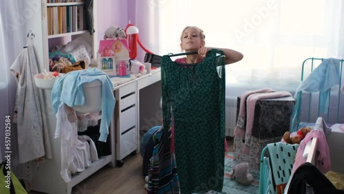 Little girl tries on dresses of her mother in messy room, chooses which one to wear, slow motion photo