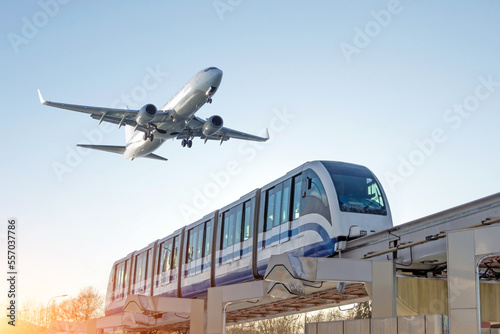 View railway track and suburban electric monorail train rushing to the departure area airfield. Passenger plane flying in sky, landing at airport. Concept of modern infrastructure transport travel.