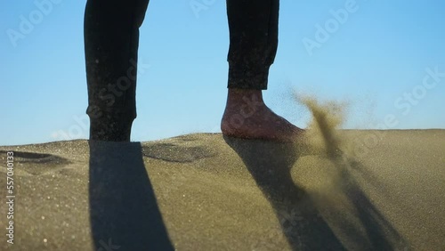 slow motion man walking barefoot on sand. camera follows male feet. coastal dunes. desert environment, lack of moisture hinders the growth of vegetation  photo