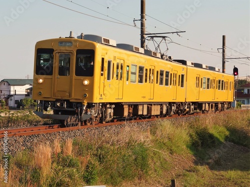 田舎を走る夕日に照らされた黄色いワンマン電車