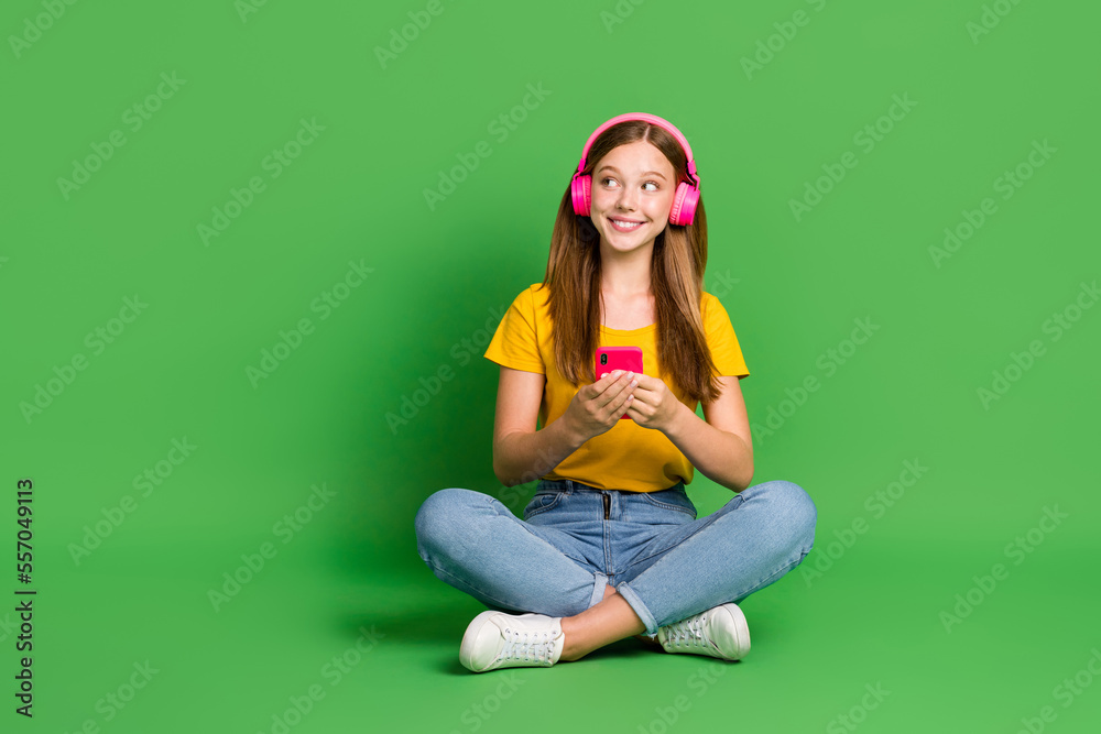 Full body photo of positive charming girl sit floor hold telephone look empty space isolated on green color background Full body photo of positive charming girl sit floor hold telephone look empty space isolated on green color background