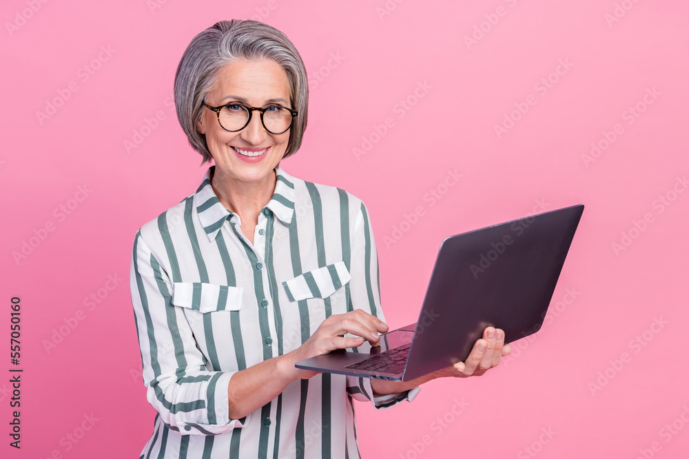 Photo of successful retired business lady white hair hold new samsung laptop online freelance copywriter job isolated on pastel pink color background Photo of successful retired business lady white hair hold new samsung laptop online freelance copywriter job isolated on pastel pink color background
