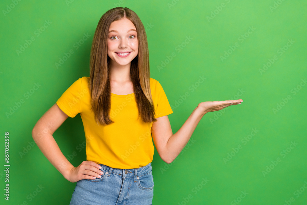 Photo of cute toothy beaming smile teen age girl wear yellow t-shirt hold palm demonstrate new cheap product sale isolated on green color background Photo of cute toothy beaming smile teen age girl wear yellow t-shirt hold palm demonstrate new cheap product sale isolated on green color background