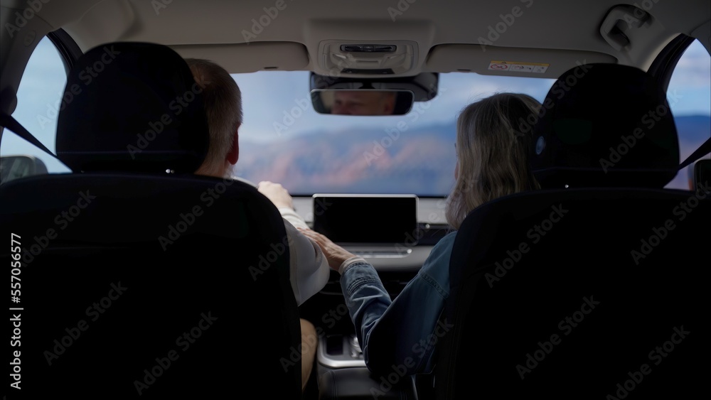 Back view of beautiful 60s mature senior grey haired Caucasian couple riding in a car, traveling together
