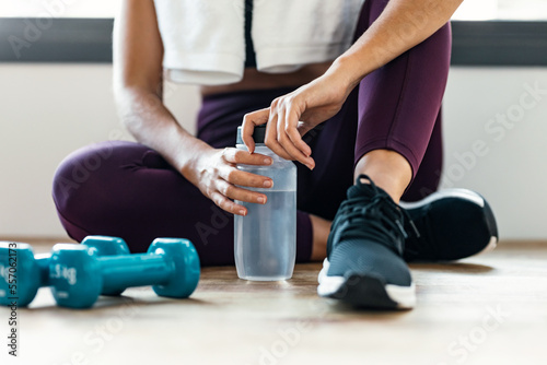 Sporty woman holding water after exercises resting in the floor at home.