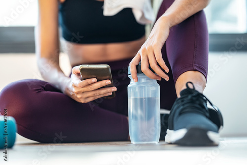 Sporty woman using her mobile phone while holding water bottle after a pilates class at home.