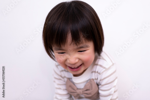 白い壁の前で笑っている3歳の女の子