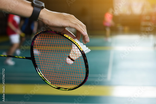 Badminton racket and old white shuttlecock holding in hands of player while serving it over the net ahead, blur badminton court background and selective focus. © Sophon_Nawit