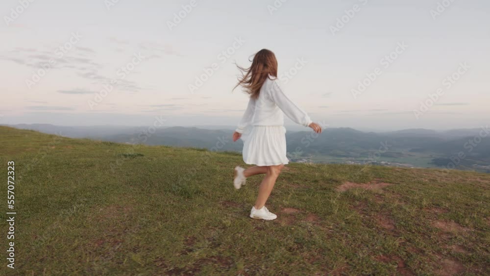 Young woman in white dress runs on the grass with sun rising on the background Young woman in white dress runs on the grass with sun rising on the background