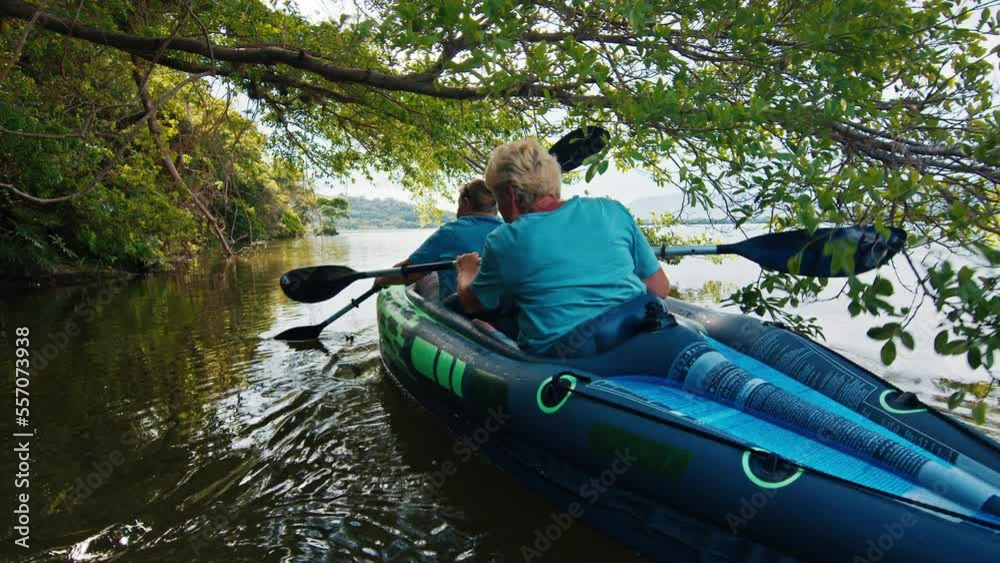 Senior women kayaking. Two elderly women paddle kayak on the fresh water lake with mangroves and trees. Elderly ladies kayaking under the trees on the calm lake Senior women kayaking. Two elderly women paddle kayak on the fresh water lake with mangroves and trees. Elderly ladies kayaking under the trees on the calm lake
