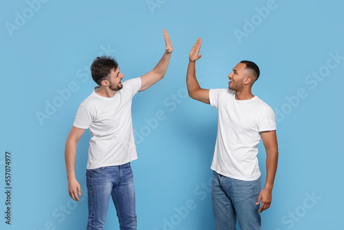 Men giving high five on light blue background photo