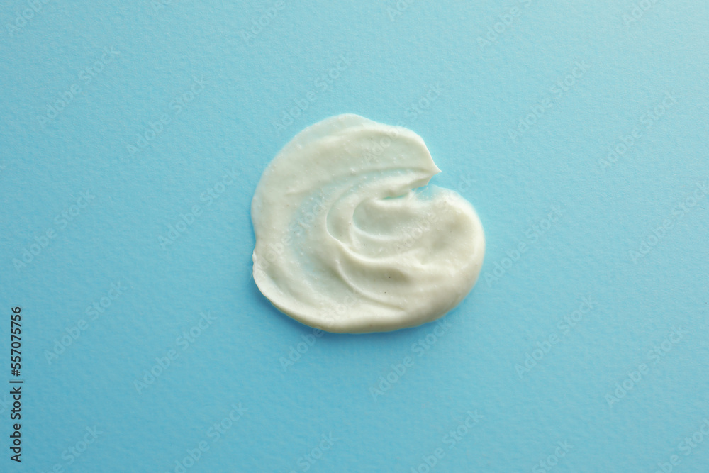 Sample facial cream on turquoise background, top view