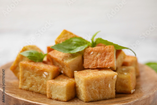 Wooden plate with delicious fried tofu, basil and sesame seeds, closeup