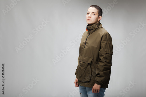 Girl with short hair wearing jacket and jeans against gray background. .