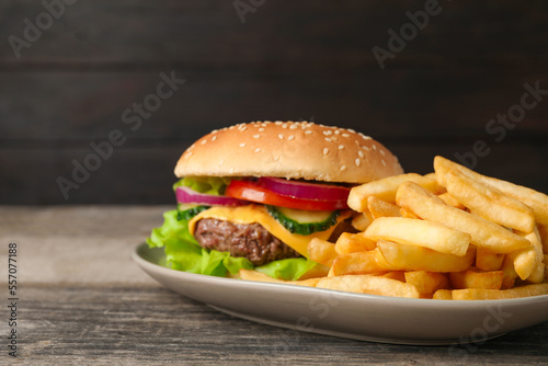 Delicious burger and french fries served on wooden table, closeup. Space for text
