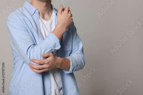 Man suffering from pain in his elbow on light grey background, closeup with space for text. Arthritis symptoms