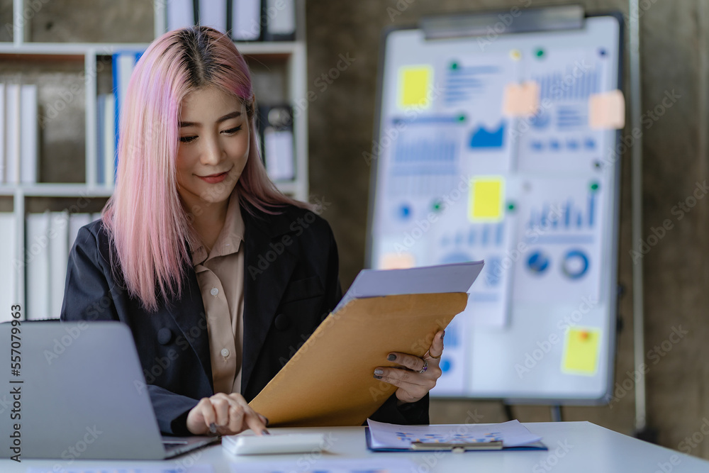 Young Asian female employee working in office with laptop and financial documents, financial accounting concept Young Asian female employee working in office with laptop and financial documents, financial accounting concept