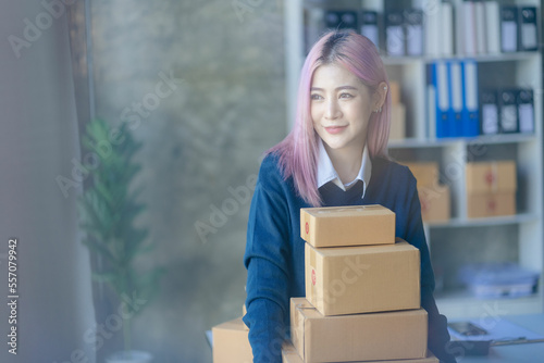 Young successful woman starting a small business, SME owner. Asian woman checking orders with smartphone and laptop, selling products online. work with boxes freelance work at home office © ArLawKa