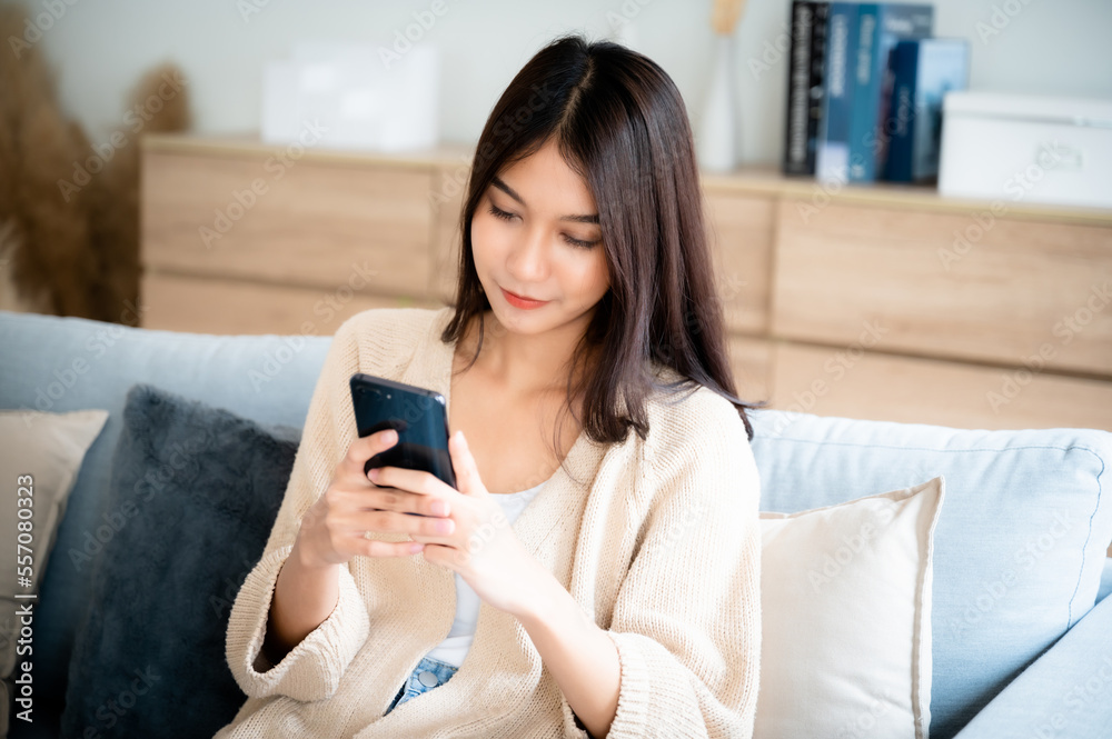 Happy young asian woman relax on comfortable couch at home texting messaging on smartphone, smiling girl use cellphone chatting, browse wireless internet on gadget, shopping online from home Happy young asian woman relax on comfortable couch at home texting messaging on smartphone, smiling girl use cellphone chatting, browse wireless internet on gadget, shopping online from home