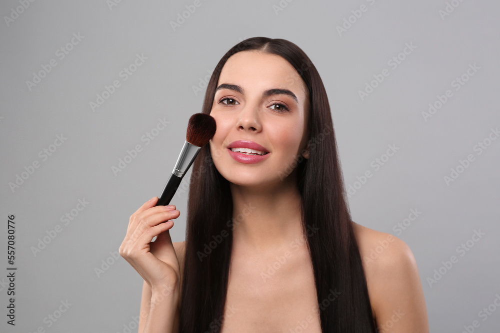 Happy woman applying makeup on light grey background Happy woman applying makeup on light grey background