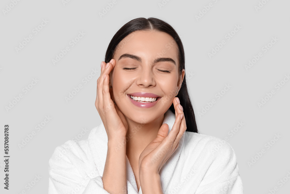Portrait of attractive young woman in bathrobe on light grey background. Spa treatment Portrait of attractive young woman in bathrobe on light grey background. Spa treatment