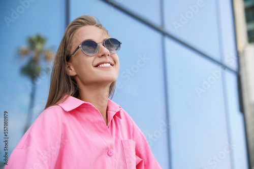 Portrait of beautiful young woman in stylish sunglasses near building outdoors, space for text