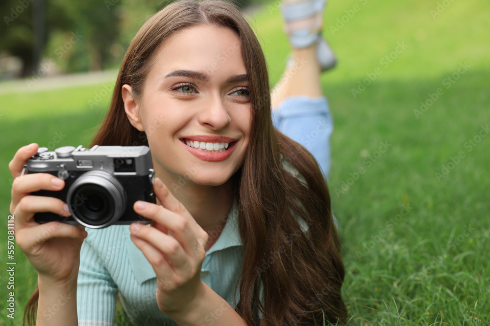 Young woman with camera on green grass outdoors, space for text. Interesting hobby