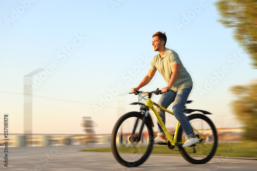 Handsome young man riding bicycle on city waterfront, motion blur effect