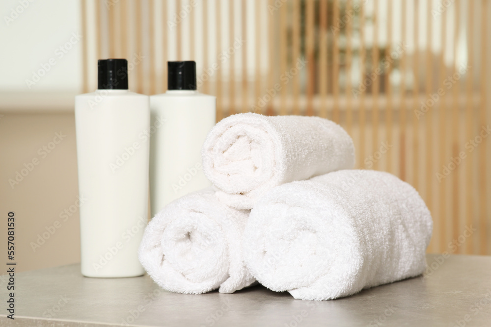 Soft folded terry towels and cosmetic bottles on light gray table indoors Soft folded terry towels and cosmetic bottles on light gray table indoors