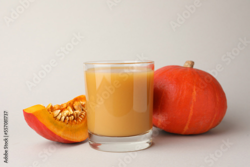 Tasty pumpkin juice in glass, whole and cut pumpkins on light background