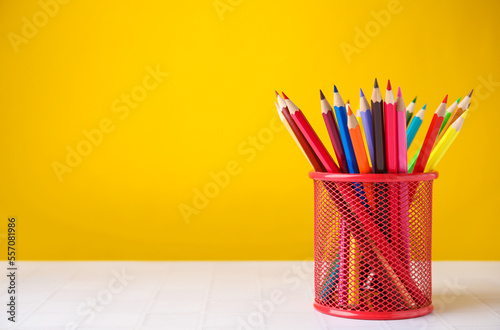Many colorful pencils in holder on light table against yellow background, space for text