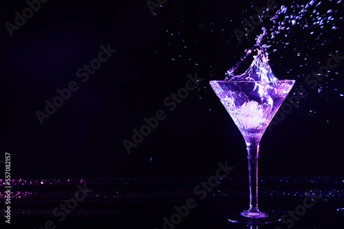 Glass of martini with ice and splashes in neon lights on dark background. Space for text