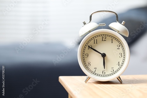 White alarm clock on wooden nightstand in bedroom, space for text