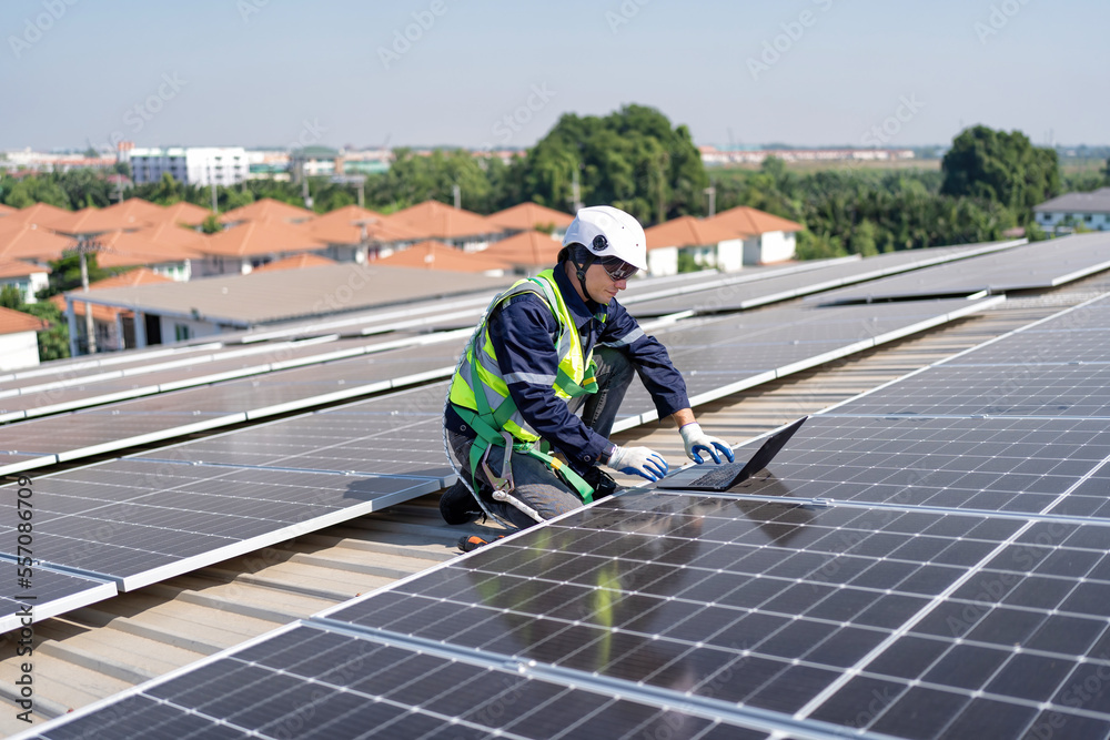 Engineer on rooftop kneeling next to solar panels photo voltaic check laptop for good installation Engineer on rooftop kneeling next to solar panels photo voltaic check laptop for good installation