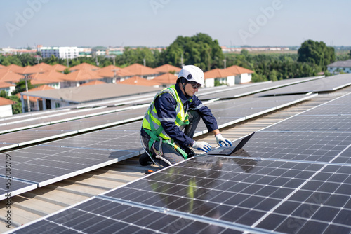 Engineer on rooftop kneeling next to solar panels photo voltaic check laptop for good installation © Tongpool