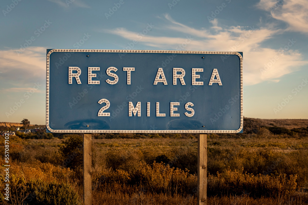 Blue road sign stating Rest Area two miles ahead against a blue sky with clouds