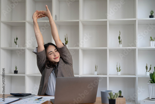 Asian businesswoman stretches her arms to relax her tired muscles from working at her desk all day at the office.
