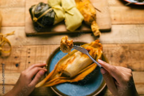 Hands of a person cutting a tamale with a fork. Tamale, typical Mexican food.