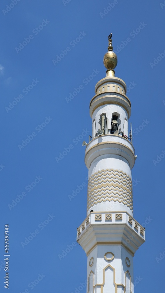 Low angle view Single Minaret of Muslim mosque on the clear blue sky background. Islam, religion and architecture, and travel concept. Mosque design in Islamic religious architectural traditions.