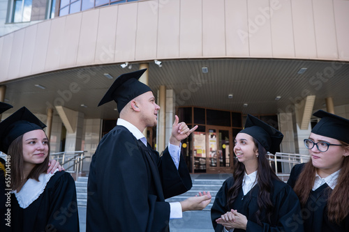 Happy students in graduate gown communicate in sign language. 