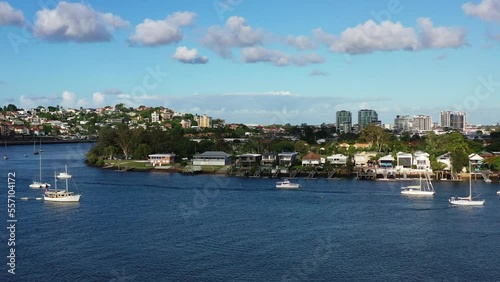 Dynamic zoom aerial view overlooking at charming Bulimba residential neighborhood capturing riverfront houses with slipway and jetty, boats moored on the water on a sunny day with blue sky. photo