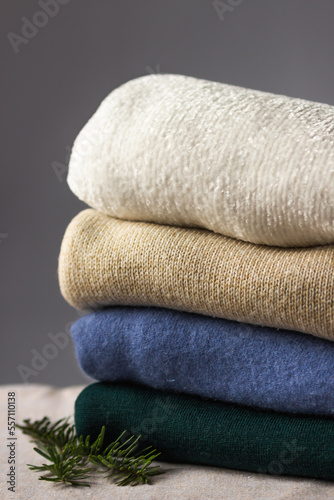 Folded knitted sweaters of different colors stacked in a pile with fir branch. Female wardrobe of winter cozy things.