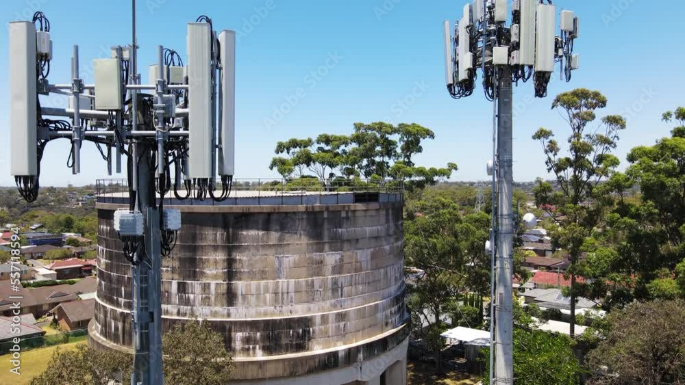 Aerial drone close up view slowly rising up and above two mobile telecommunication cell towers next to a water tower reservoir at Padstow Heights in south western Sydney, NSW Australia Aerial drone close up view slowly rising up and above two mobile telecommunication cell towers next to a water tower reservoir at Padstow Heights in south western Sydney, NSW Australia