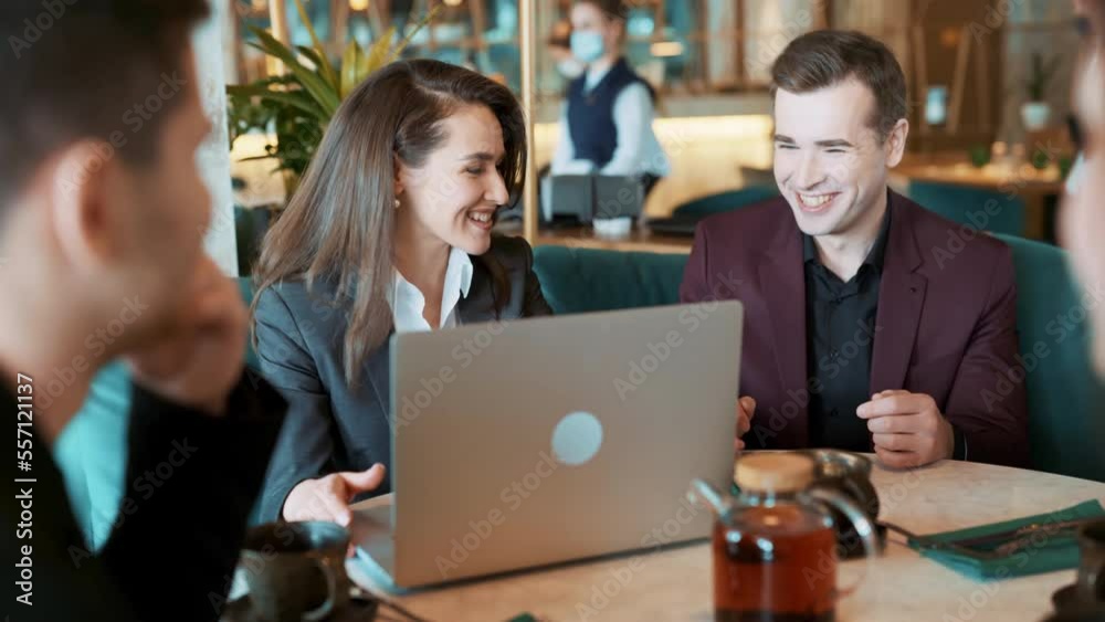 Group of suit wearing colleagues discussing working situation sitting at table in cafe with laptop. Casual coworkers having sparkling conversation in reastaurant. Concept of teambuilding, leisure.
