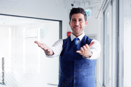 Smiling young businessman standing with open hands in office.