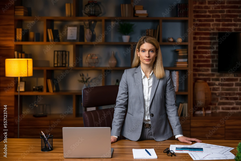 Portrait of a serious businesswoman standing at the table in office and looking at camera