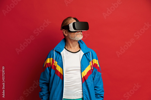 Focused Man Trying VR. Portrait of Senior Man Discovering New Technologies Wearing Virtual Reality Headset, Futuristic 3d Vision. Indoor Studio Shot Isolated on Red Background 